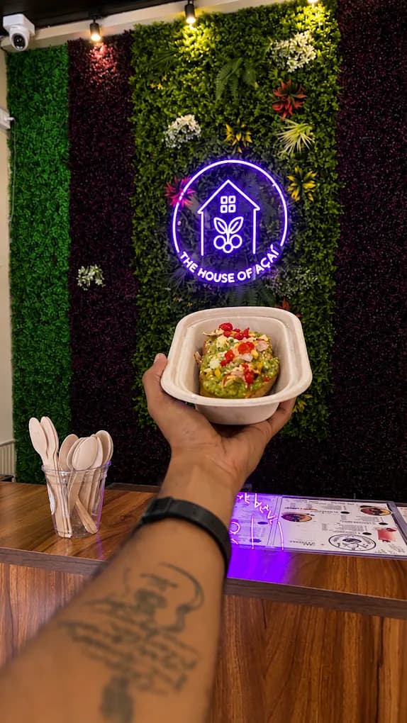 An avocado crunch bowl held in front of the café's moss wall, lit by the neon logo